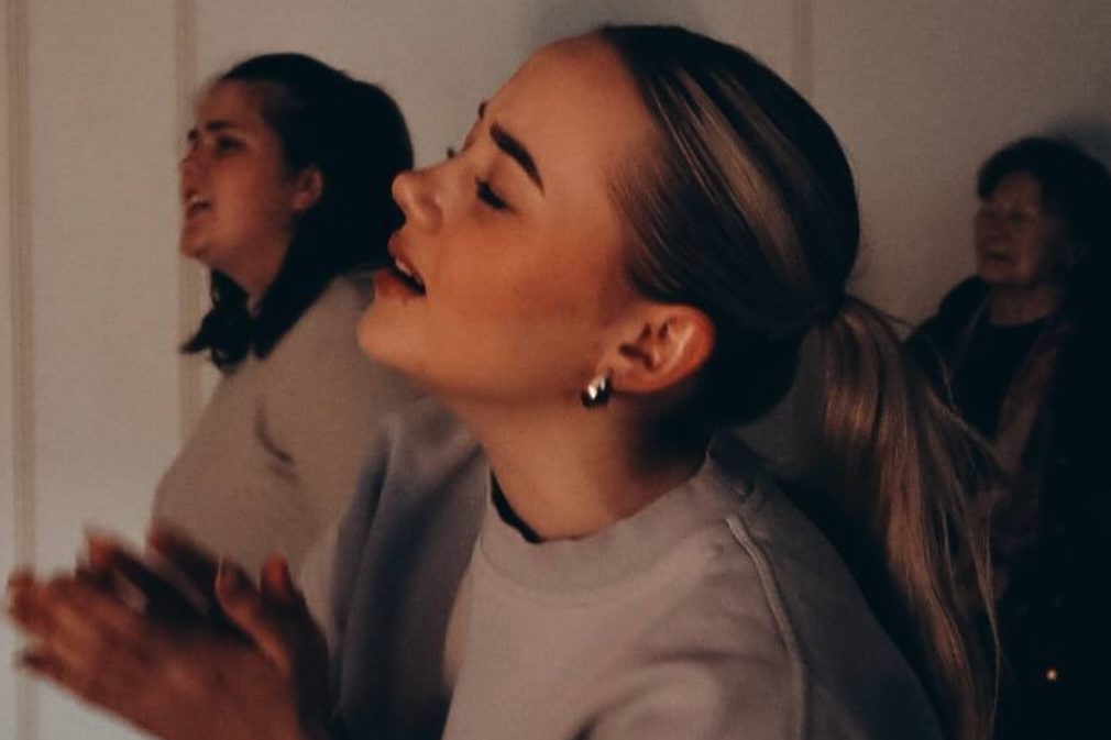 Zwei junge Frauen singen im Gottesdienst, die vordere im Profil mit geschlossenen Augen.