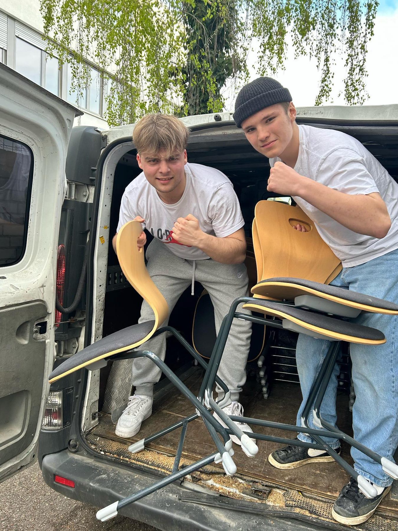 Zwei junge Männer heben Stühle aus einem weißen Transporter.