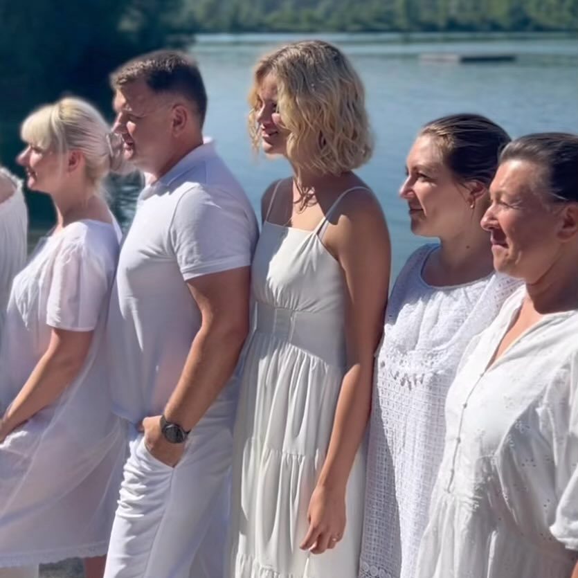 Menschen in weißer Kleidung stehen in einer Reihe am sonnigen Seeufer.