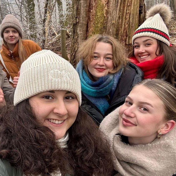 Junge Leute lachen bei einem Gruppenfoto im winterlichen Wald in die Kamera.