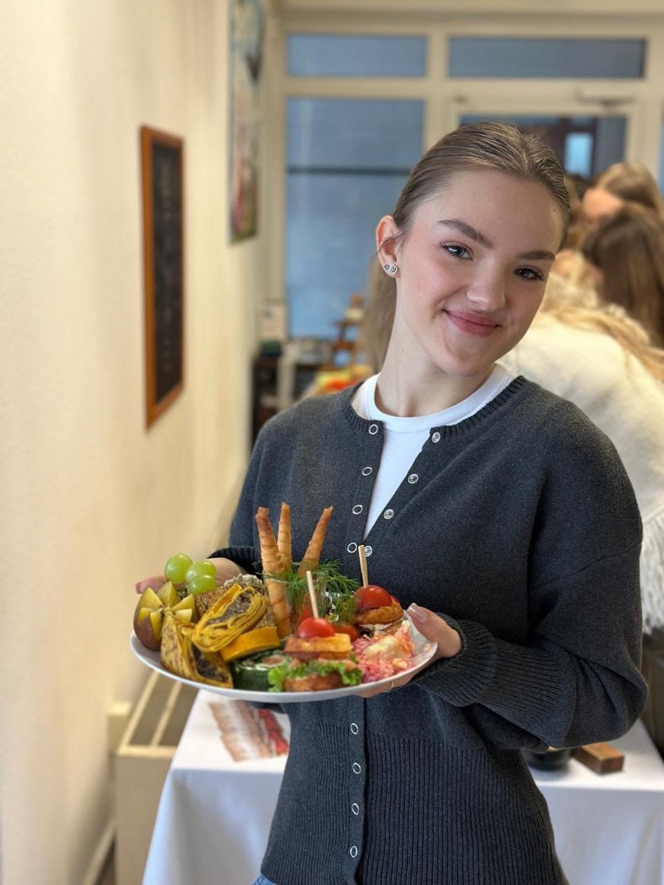 Eine junge Frau hält lächelnd einen Teller mit Häppchen, hinter ihr ein Buffet.