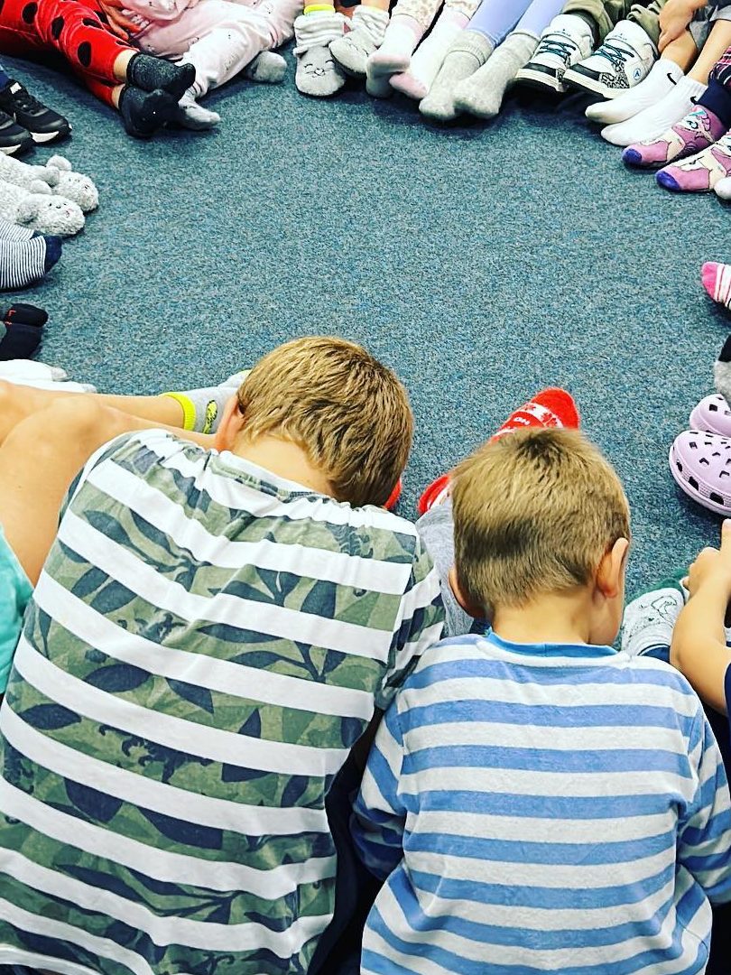 Kinder sitzen in bunten Socken im Kreis auf einem Teppich, von hinten gesehen.